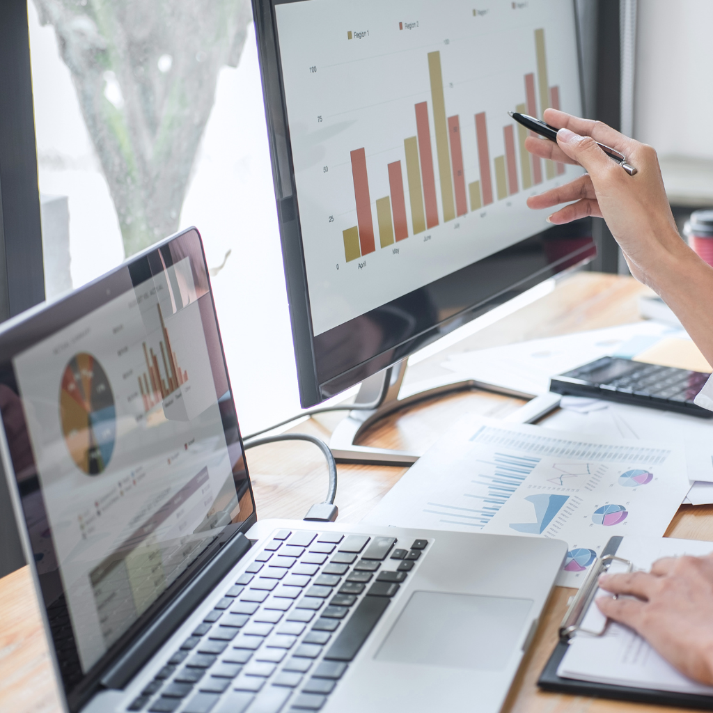 two screens with data charts and a women pointing a pen at one of the charts on the screen
