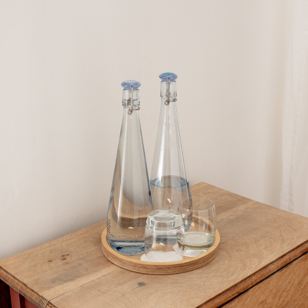 Glass water bottles and glasses on a light wood night stand